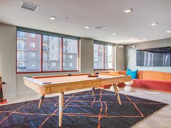 A pool table in a room with a view of apartment buildings outside the window.